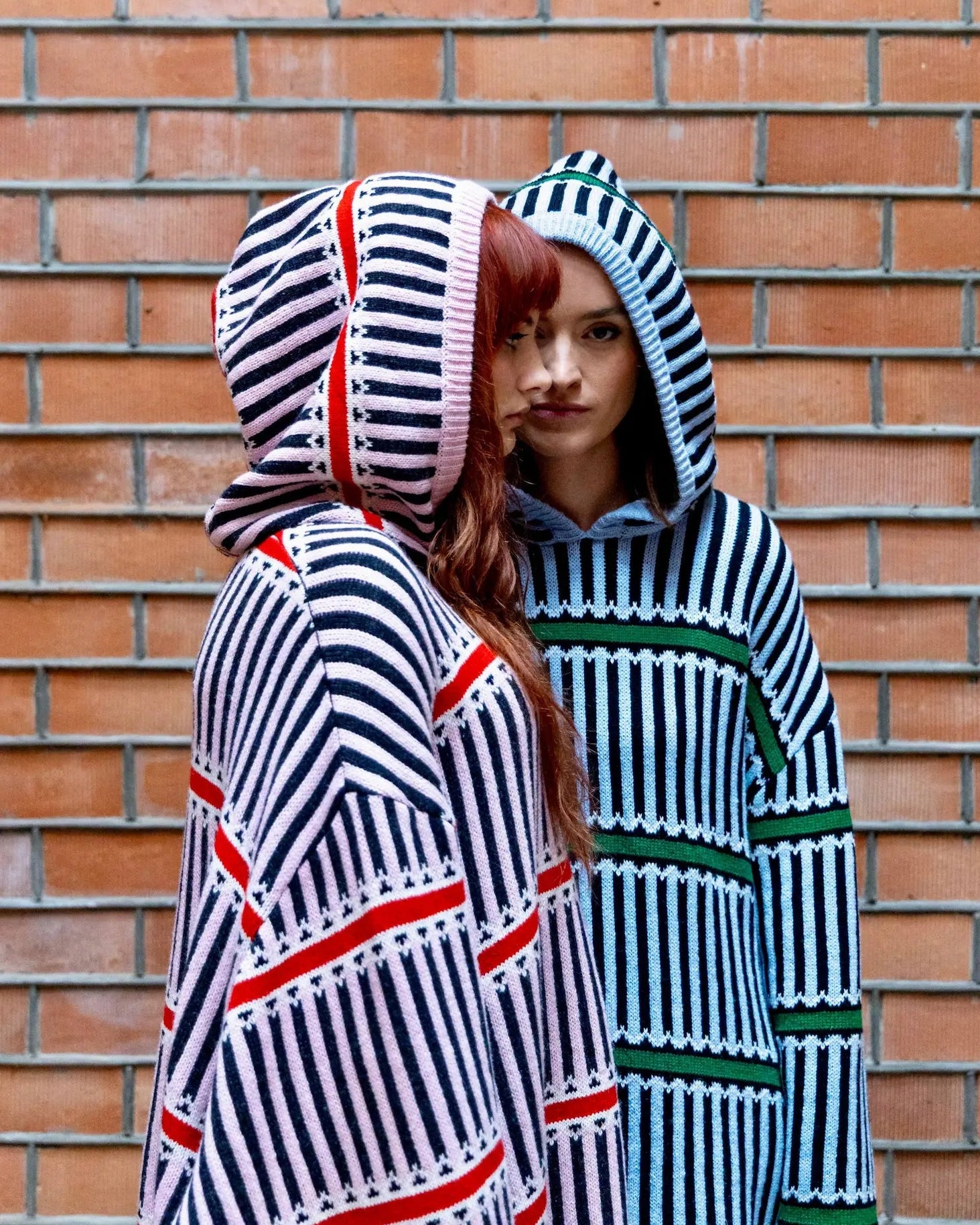 Two people wearing striped hoodies against a brick wall.