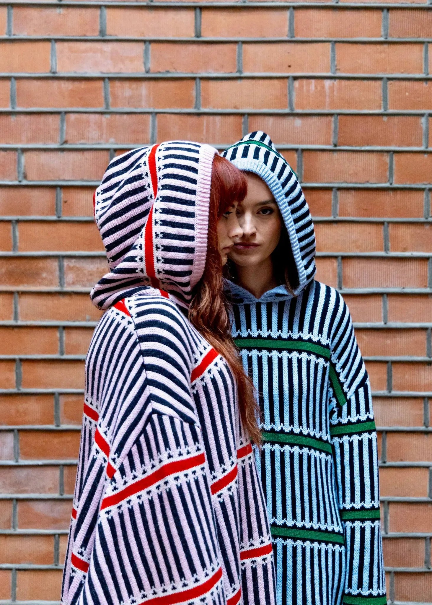 Two people wearing striped hoodies against a brick wall.