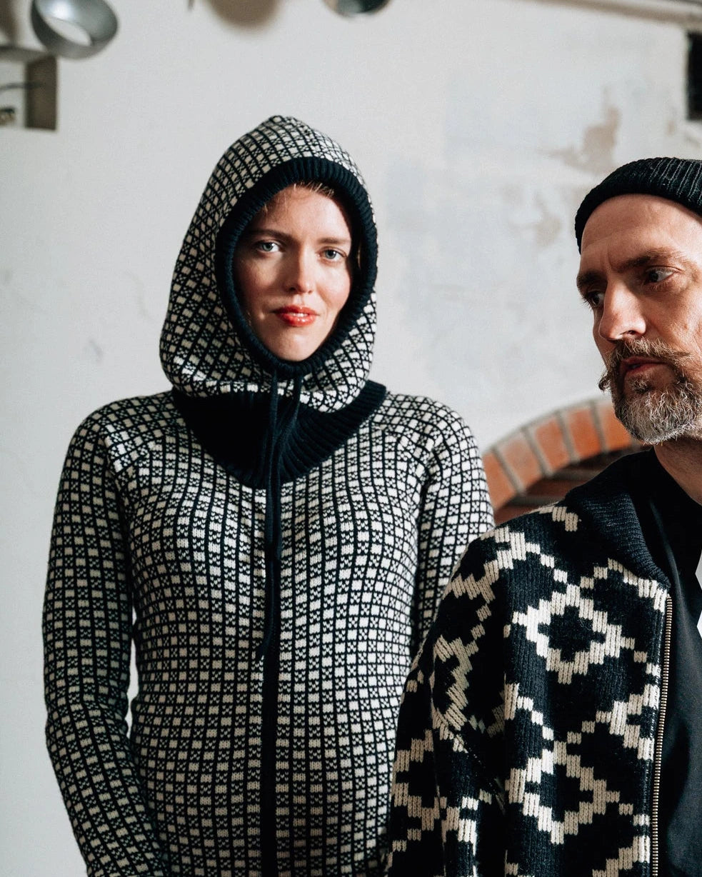Two people wearing patterned kintwear and a balaclava in an indoor setting.