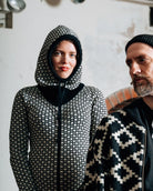 Two people wearing patterned kintwear and a balaclava in an indoor setting.